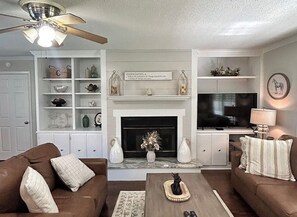 A living room with a fireplace, a ceiling fan, and a television. - 3-bedroom house in delightful Valdosta with pool, jacuzzi, and cool AC. (Valdosta)