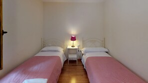 A small, clean room with two single beds, a bedside table with a lamp, and a white wall. - Pondiellos 34 - tucasaenlospirineos (Escarrilla)