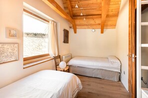 Une chambre avec deux lits, une fenêtre avec des rideaux, un radiateur et un plafond en bois.