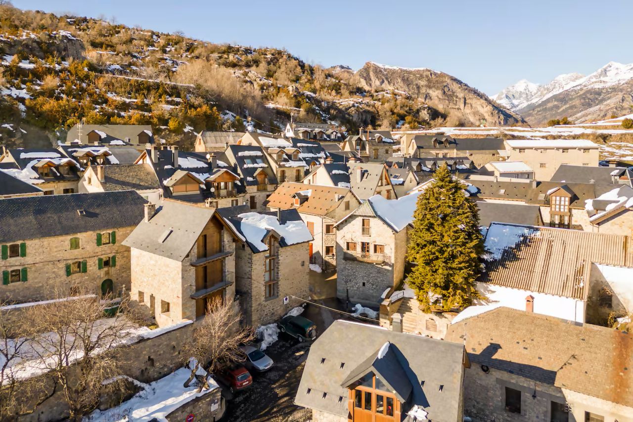 A village with traditional stone buildings, narrow streets, and a prominent tree.