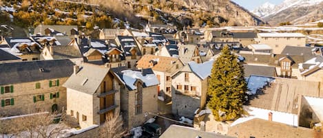 A village with traditional stone buildings, narrow streets, and a prominent tree.