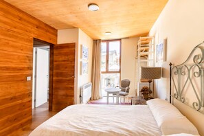 Een slaapkamer met een houten plafond, een bed, een stoel, een tafel en een raam met gordijnen.