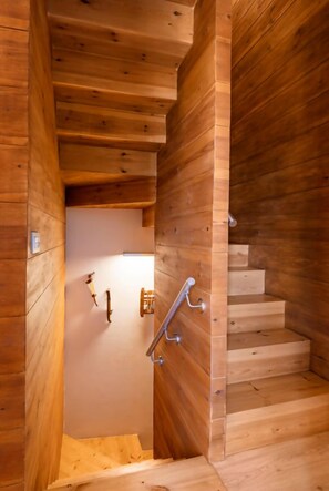 A wooden staircase with a metal handrail leading to a room with a white wall and a door. - El Pajar de la Leña - tucasaenlospirineos (Sandinies)