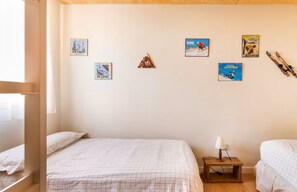 A bedroom with two beds, a wooden nightstand with a lamp, and ski-themed wall art. - El Pajar de la Leña - tucasaenlospirineos (Sandinies)