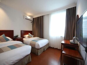 A hotel room with two beds, a desk, a TV, and a window with curtains.