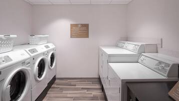 A laundry facility with three washing machines, a drying machine, and a sign indicating free guest laundry.