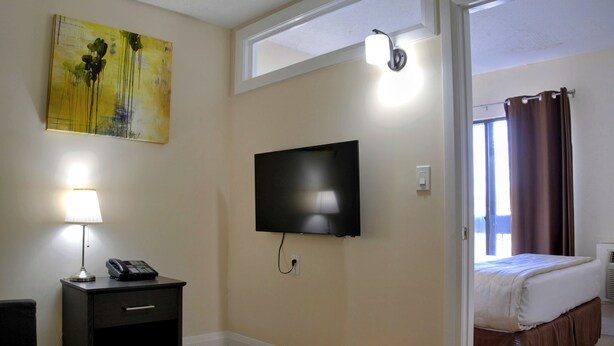 Ein Hotelzimmer mit einem Bett, einem an der Wand befestigten Fernseher, einem Nachttisch mit Lampe und einem Wandbild.