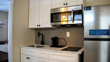 A compact kitchen with white cabinets, a stainless steel microwave, a coffee maker, and a refrigerator.