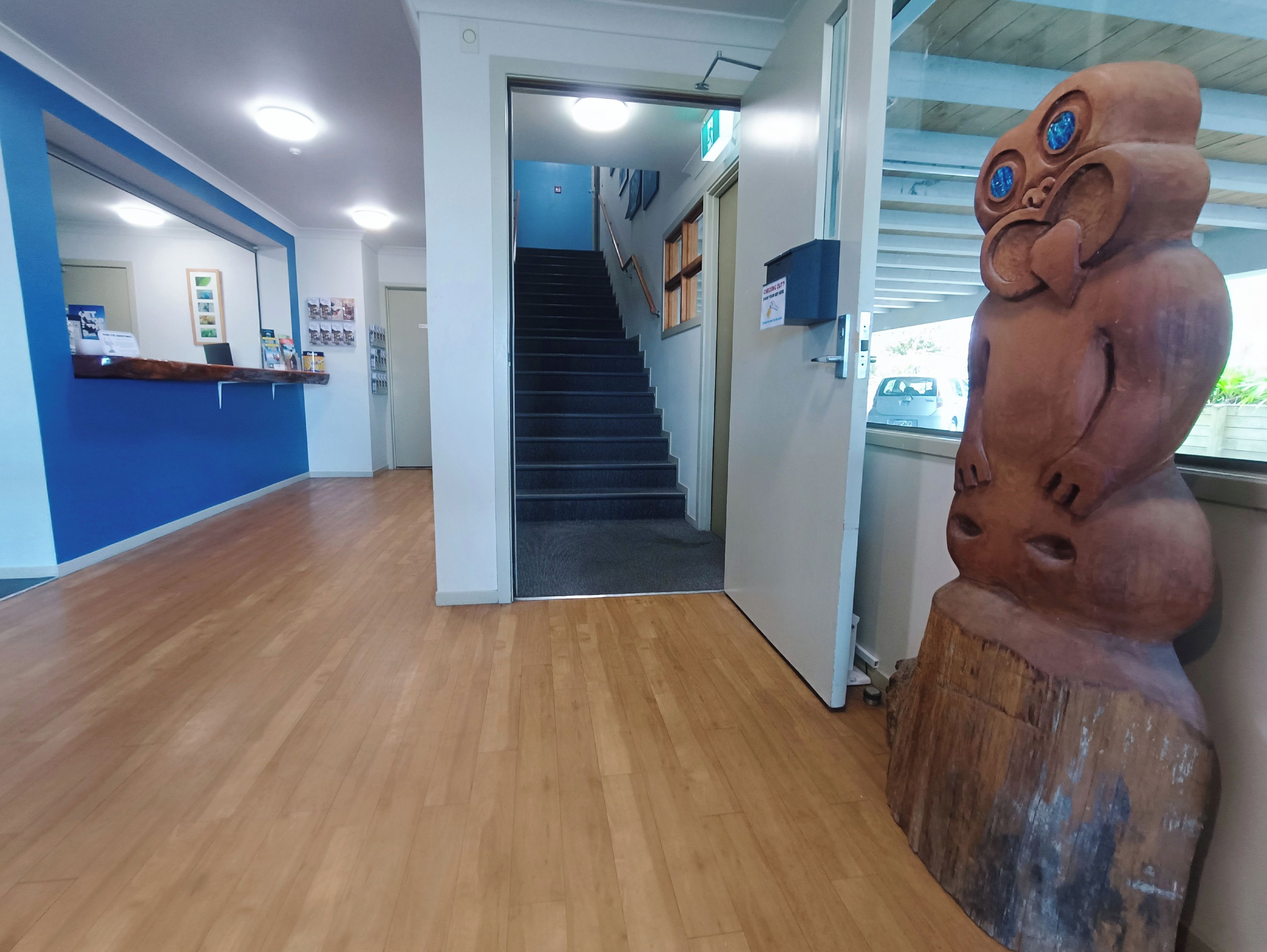 Un área de recepción con suelo de madera, un mostrador de recepción, una escalera y una escultura decorativa.