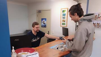 A person handing over a card to another person at a counter with a sign that reads 'PUSH FOR ASSISTANCE'.