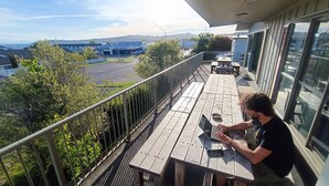 A balcony with a view of a road and buildings, a wooden table, and a person using a laptop.