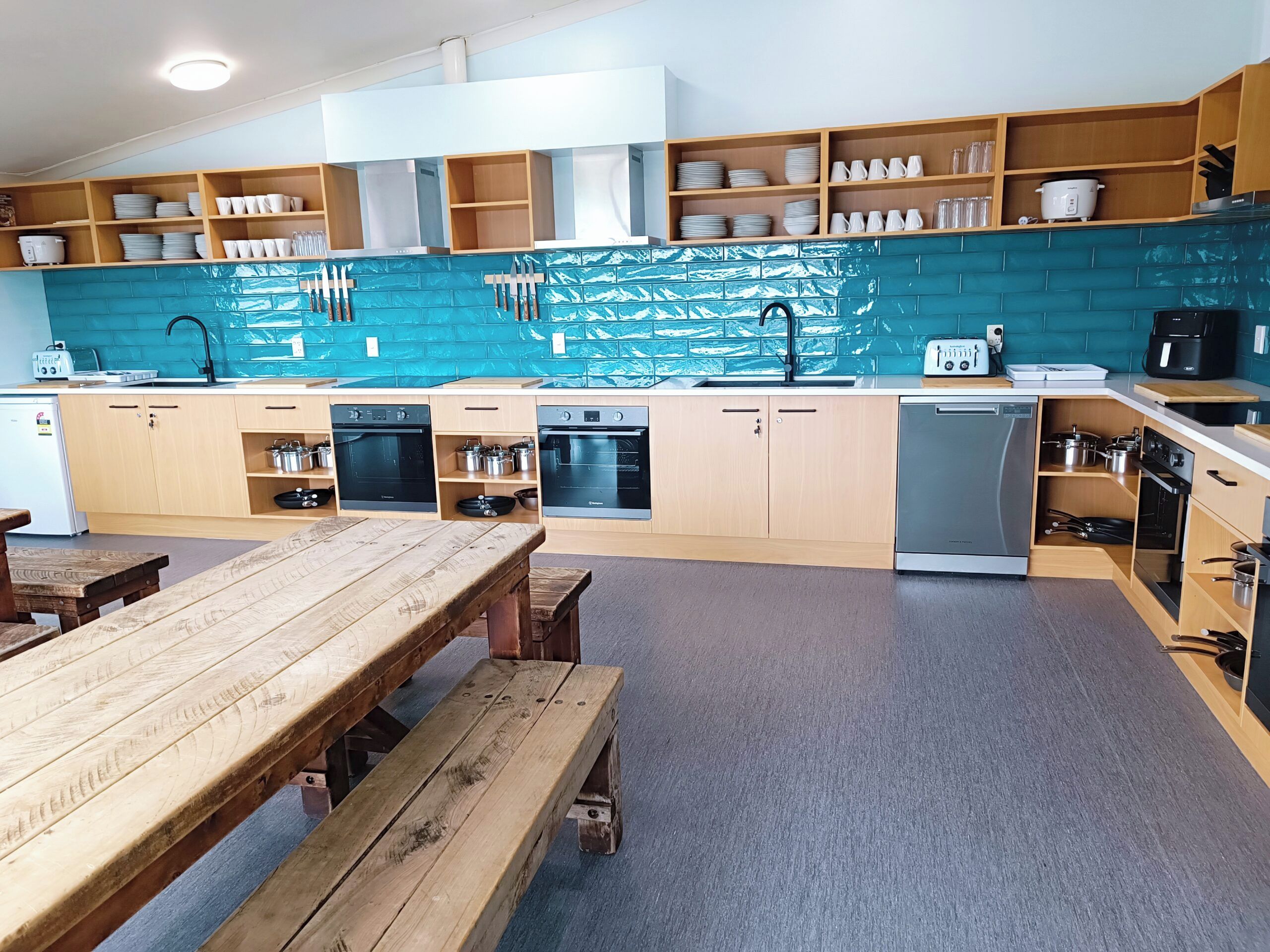A modern kitchen with wooden cabinets, a blue backsplash, and a dining area with a wooden table and benches.