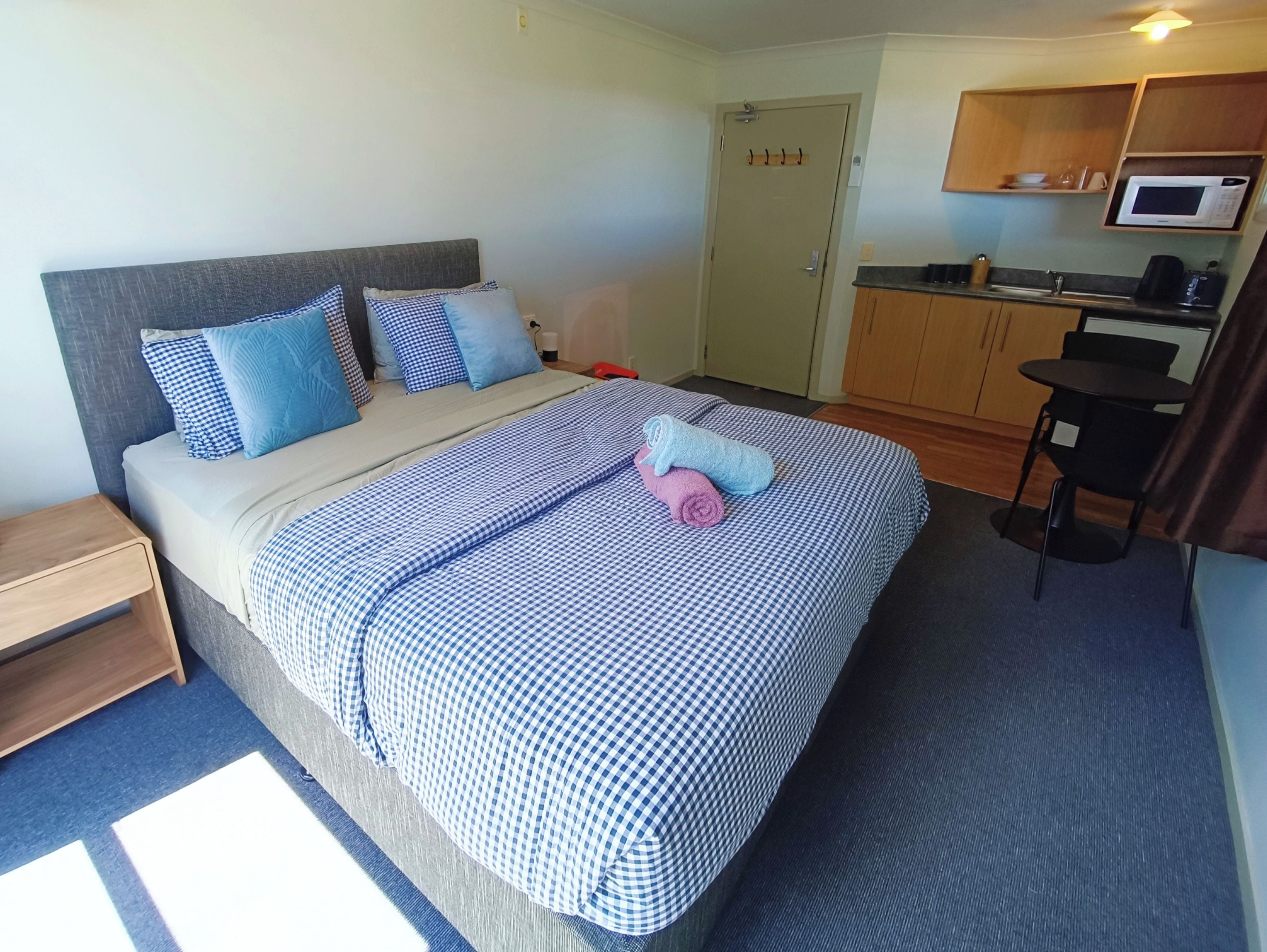 Habitación de hotel con cama, mesita de noche, escritorio pequeño, microondas y kitchenette.