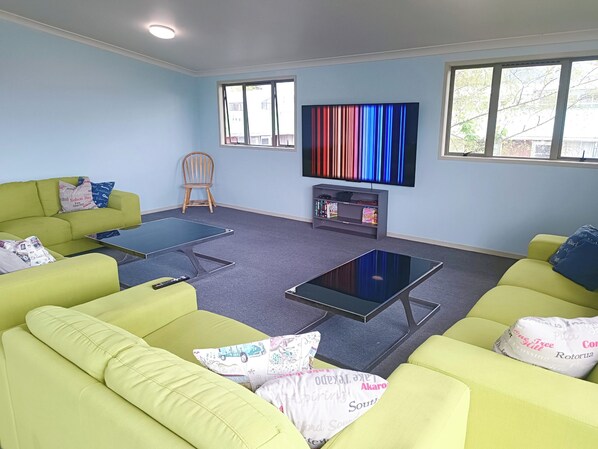 A living room with green sofas, a flat-screen TV, and a bookshelf.