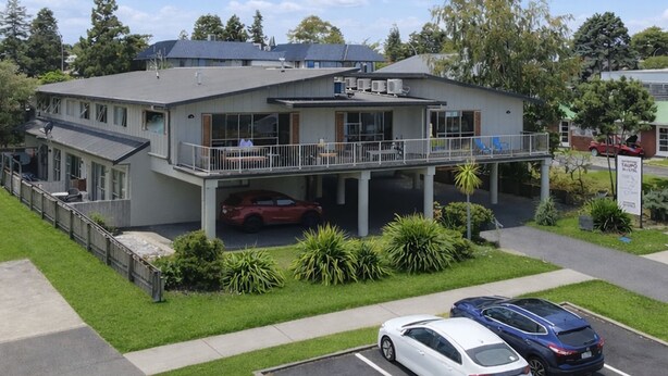 A two-story building with a covered parking area, a balcony, and a sign indicating a hotel.