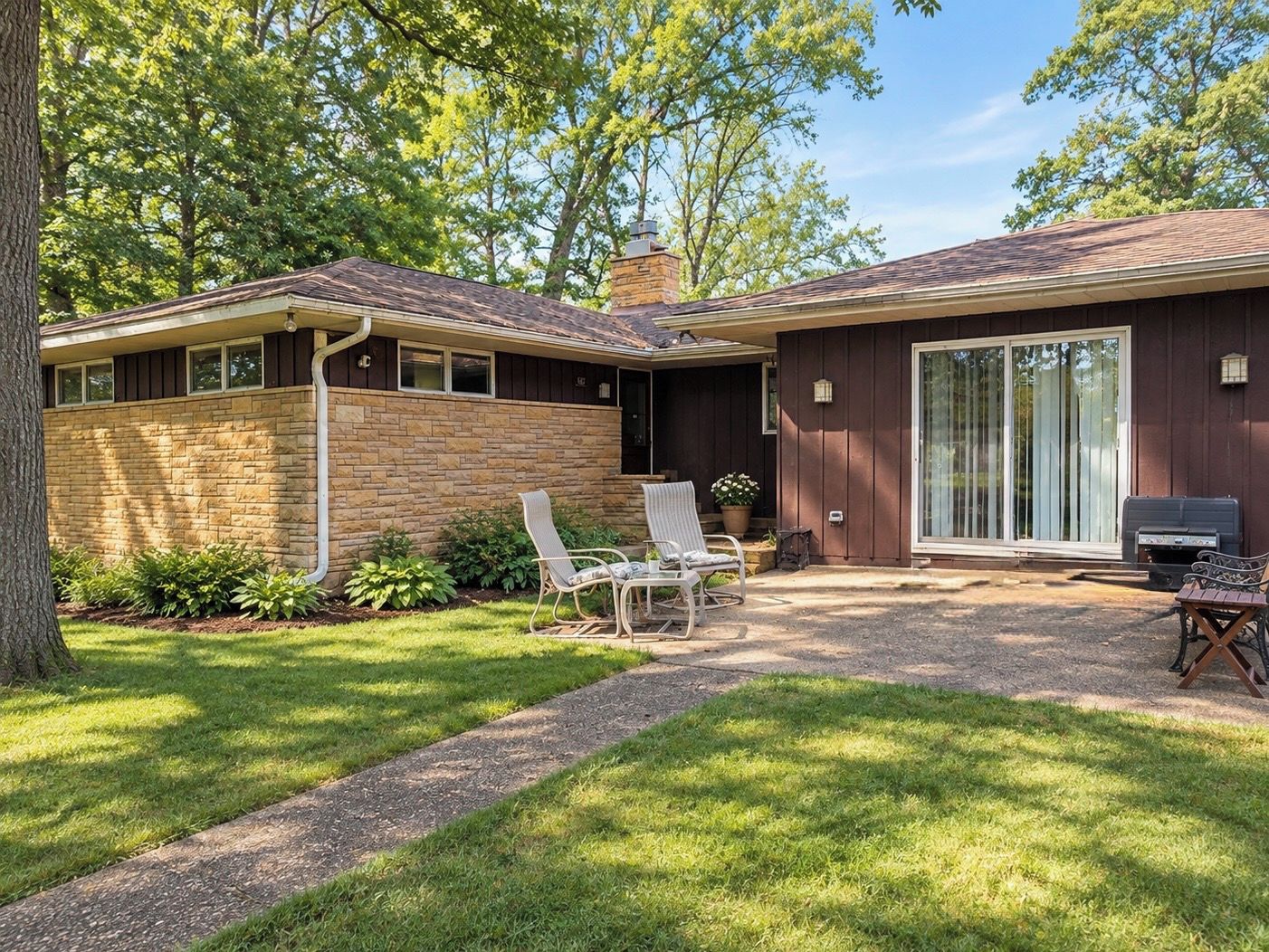 A house with a stone facade, a covered patio with outdoor furniture, and a large sliding glass door.
