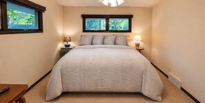 Une chambre à coucher comprenant un lit, deux tables de chevet, une commode, une fenêtre et un luminaire au plafond.