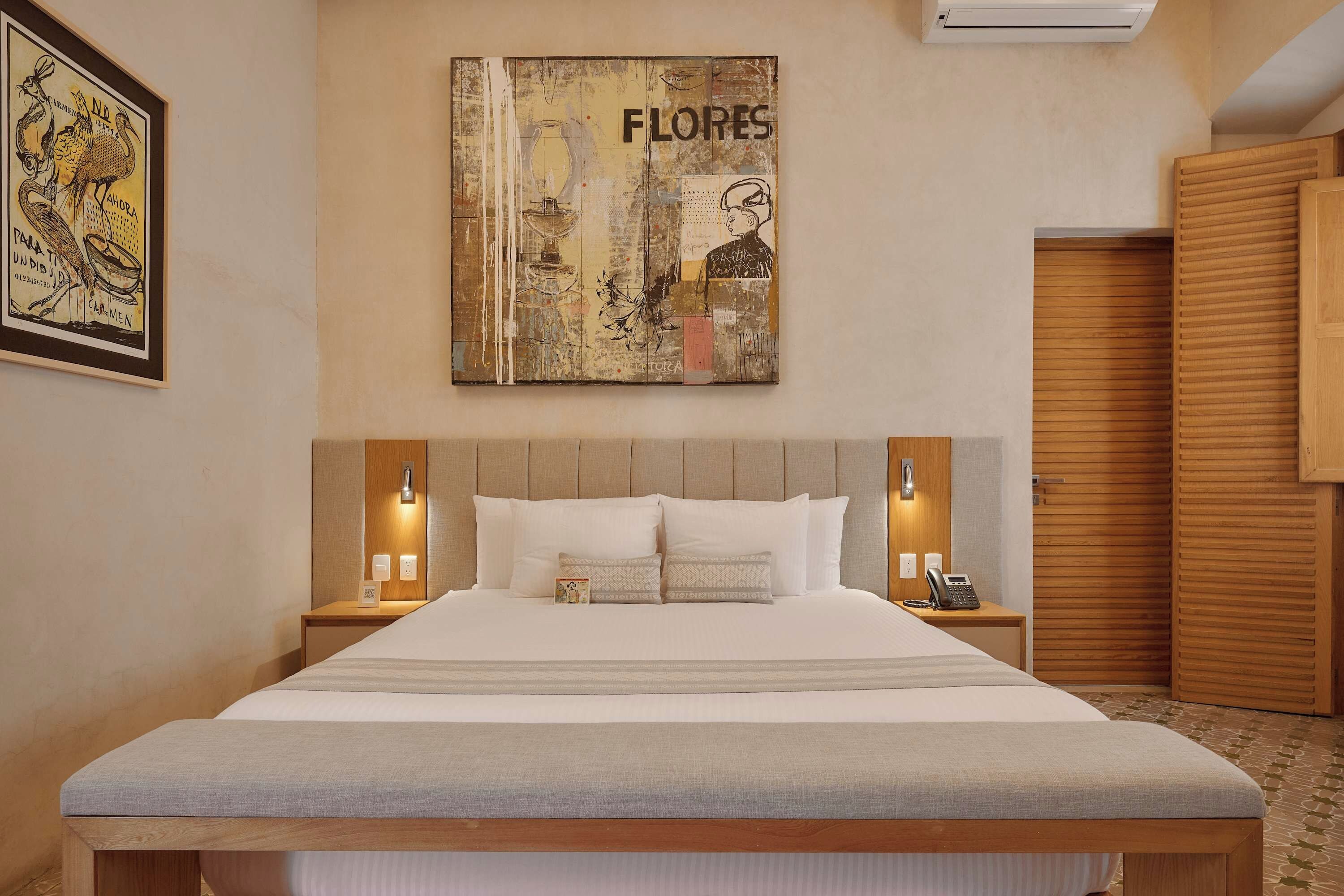 Een hotelkamer met een groot bed, twee nachtkastjes met lampen, een houten garderobe en een schilderij aan de muur.