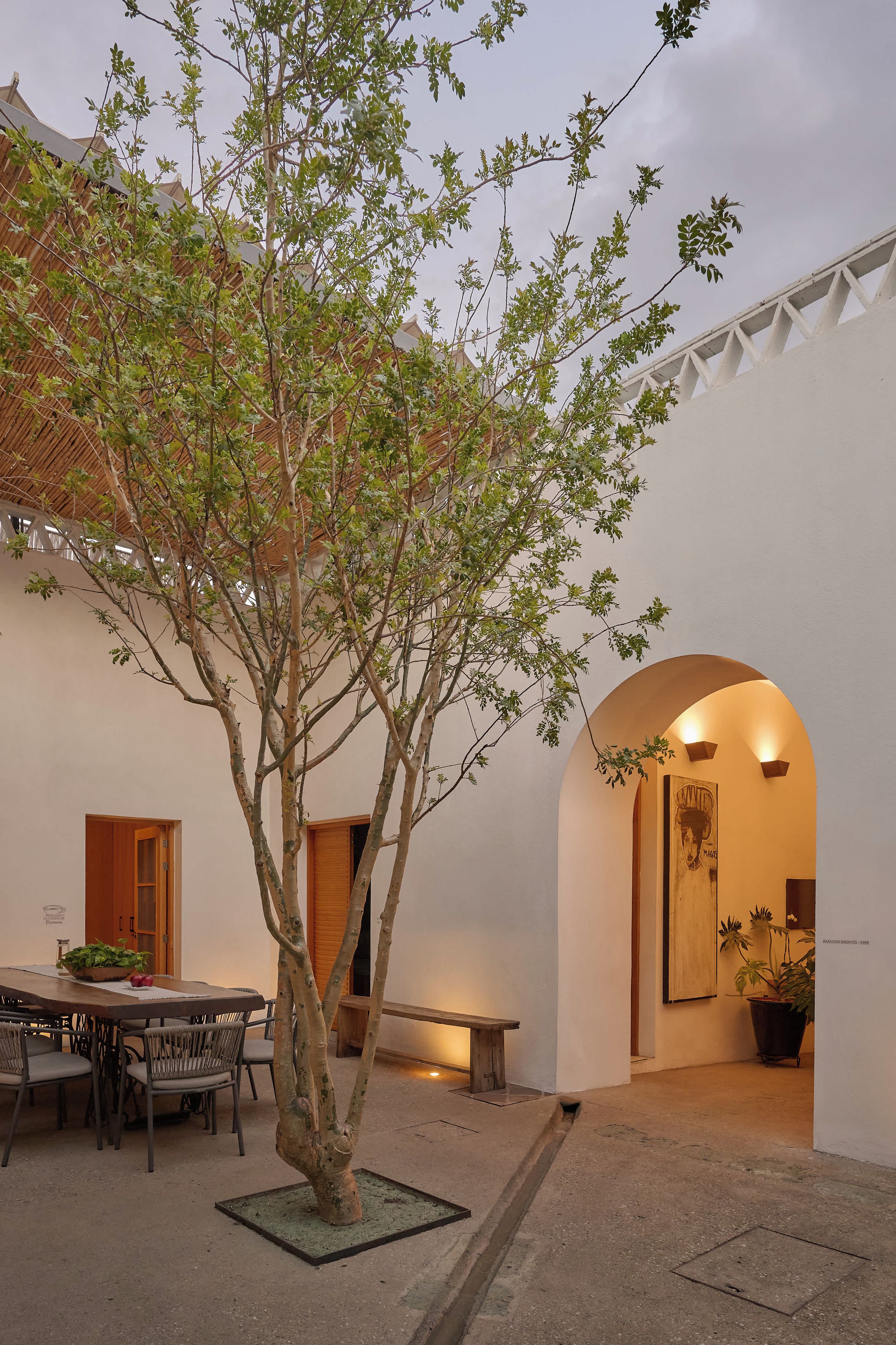 A courtyard with a tree, a dining table with chairs, and a bench.