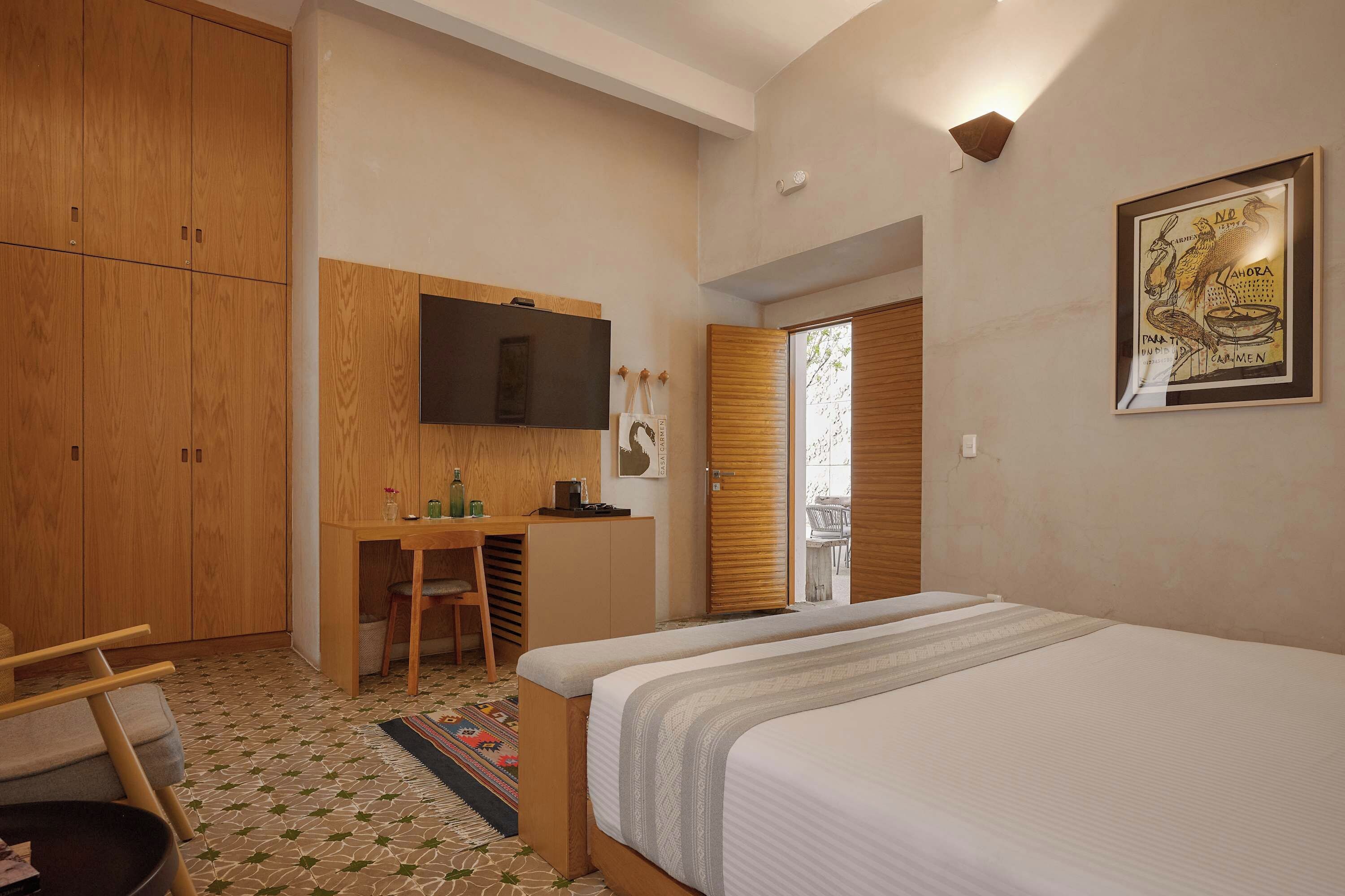A hotel room with a bed, a desk with a chair, a wardrobe, and a television.