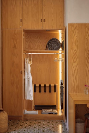 Een houten garderobe met een kledingroede, een spiegel en een klein tafeltje met een vaas.