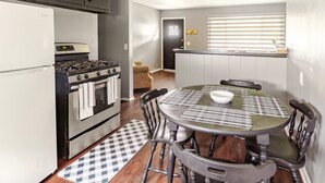 Cocina funcional con estufa, horno y refrigerador. Hay una mesa de comedor con sillas y un tapete a cuadros.