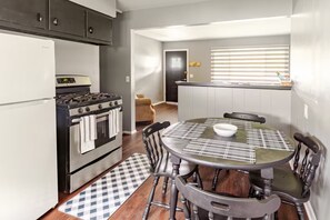 A compact kitchen with a stove, oven, and refrigerator. There is a dining table with chairs and a checkered rug.
