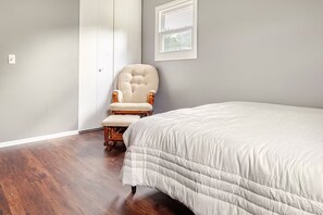 A bedroom with a bed, a chair, a wardrobe, and a window.
