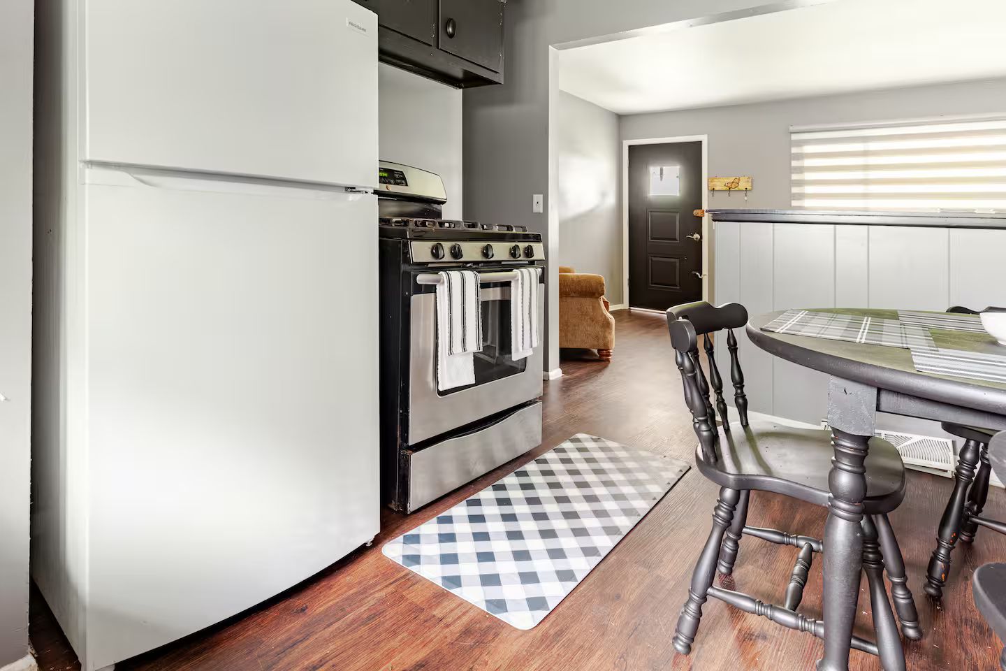 Une cuisine compacte équipée d’un réfrigérateur, d’une cuisinière et d’un coin repas agrémenté d’un tapis à carreaux.