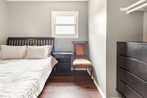 A bedroom with a bed, a nightstand, a chair, a desk, and a wardrobe.