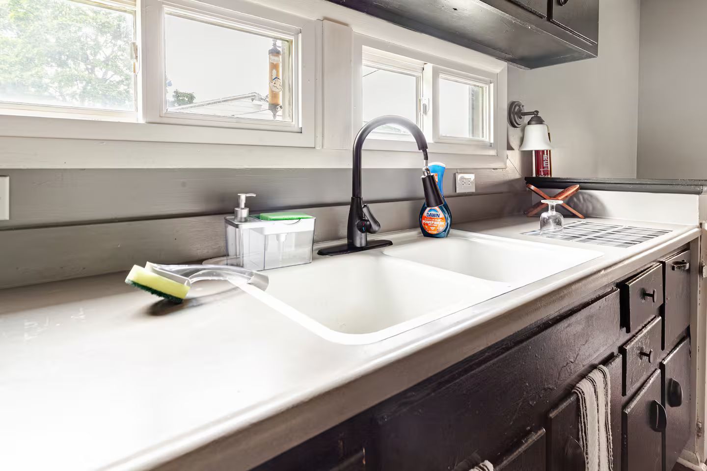A kitchen with a white countertop, a black faucet, a soap dispenser, and a bottle of Dawn dish soap.