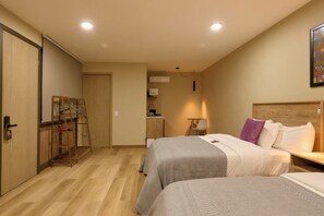Een hotelkamer met twee bedden, een bureau, een stoel, een klein tafeltje en een kitchenette.