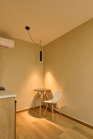 A small, modern room with a round table and a single white chair, a white air conditioning unit on the wall, and a pendant light fixture. - Vibrant Oaxaca Suites Steps from Santo Domingo (Oaxaca de Juárez)