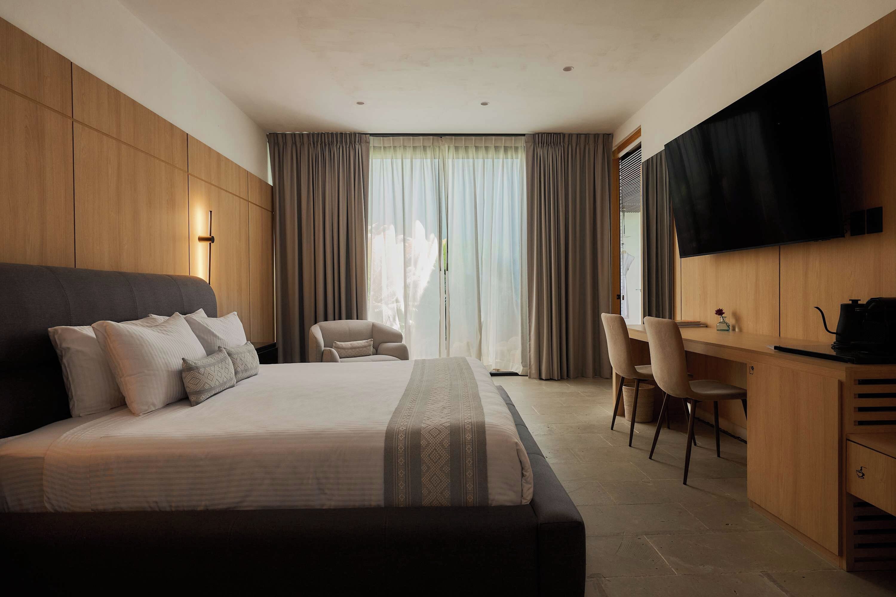 Une chambre d’hôtel moderne équipée d’un grand lit, d’un bureau, d’une chaise et d’un téléviseur à écran plat fixé au mur.