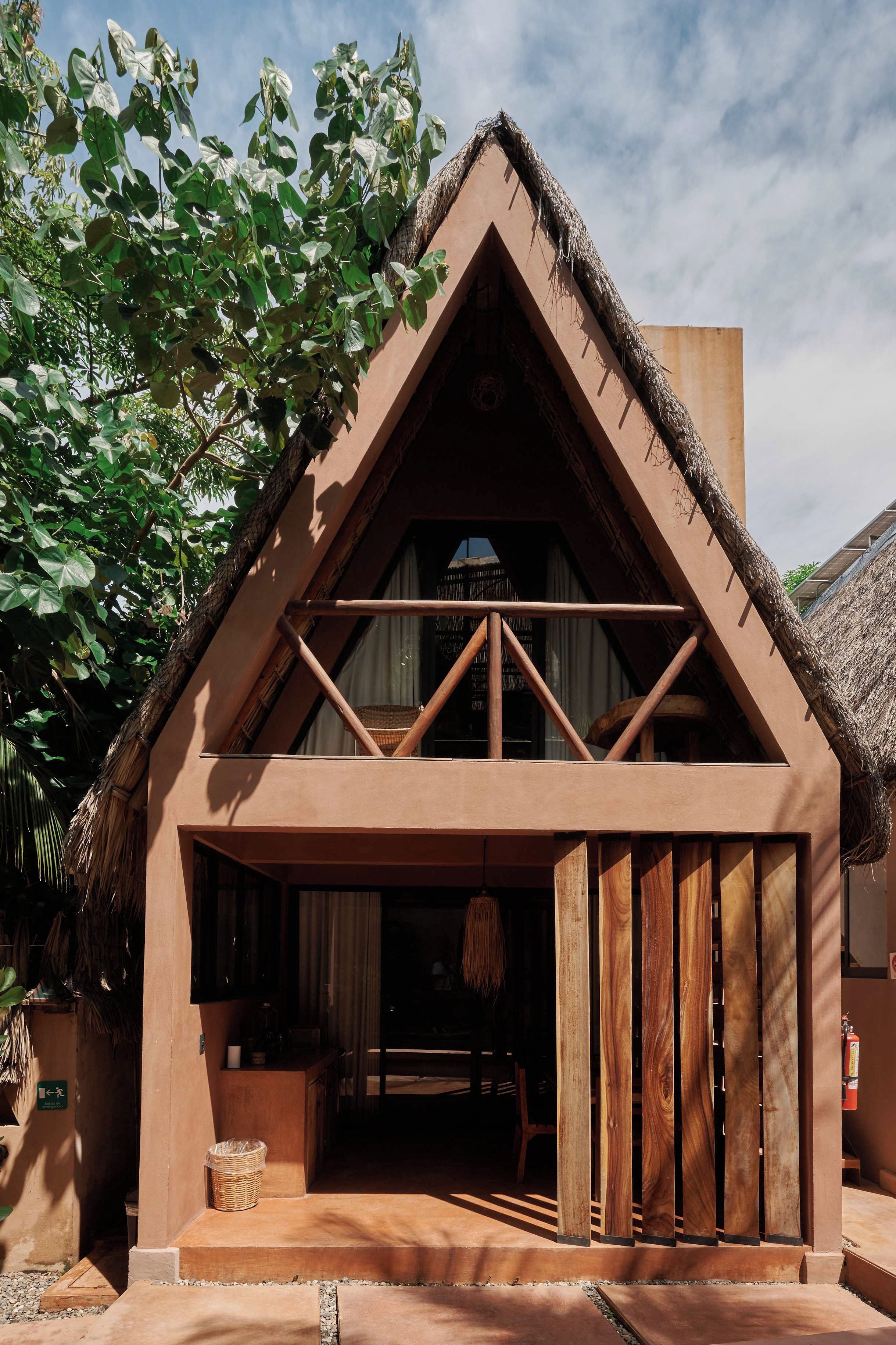 A rustic building with a thatched roof, a wooden balcony, and a door leading to an interior space.