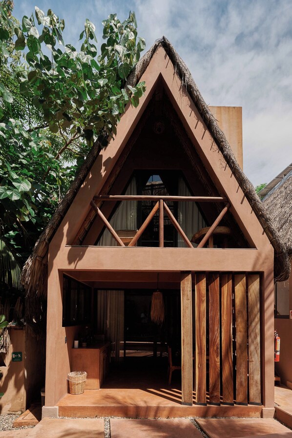A rustic building with a thatched roof, a wooden balcony, and a door leading to an interior space.