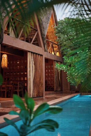 A poolside area with a wooden structure, a hanging light fixture, and a clear blue pool.