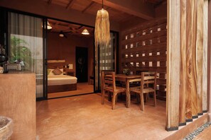 A room with a bed, a dining table with chairs, a hanging light fixture, and a wooden wall with a grid pattern.