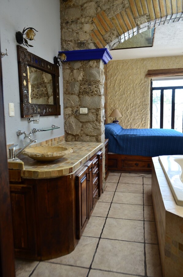 Un baño con pared de piedra, un lavabo, un espejo y una cama con cubierta azul.