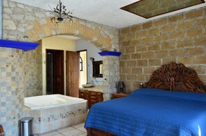 Une chambre avec un grand lit, une baignoire et un mur en pierre.