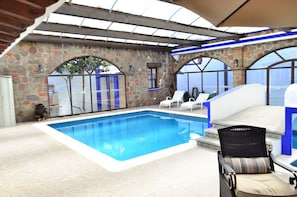 Une piscine intérieure avec des murs en pierre, un plafond en verre et des chaises longues.