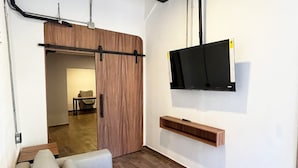 Moderni huone, jossa on sohva, seinälle asennettu televisio ja puinen ovi.