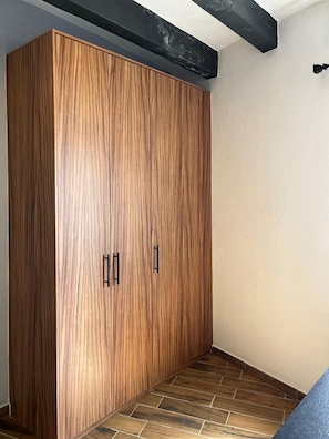 A room with a large wooden wardrobe, a tiled floor, and a black beam on the ceiling.