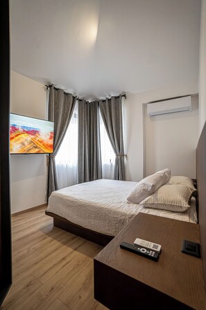 Ein Hotelzimmer mit Bett, Wandfernseher, Nachttisch mit Fernbedienung und Klimaanlage.