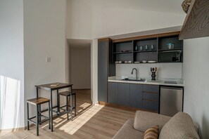 A modern kitchen with a built-in dishwasher, a dining area with a small table and two stools, and a sofa in the living area. - Laurelian 4 · Larea · Private suite near downtown (Oaxaca de Juárez)