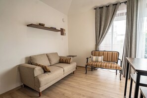 Ein Wohnzimmer mit einer Couch, einem Sessel, einem Holztisch und einem Fenster mit Vorhängen.
