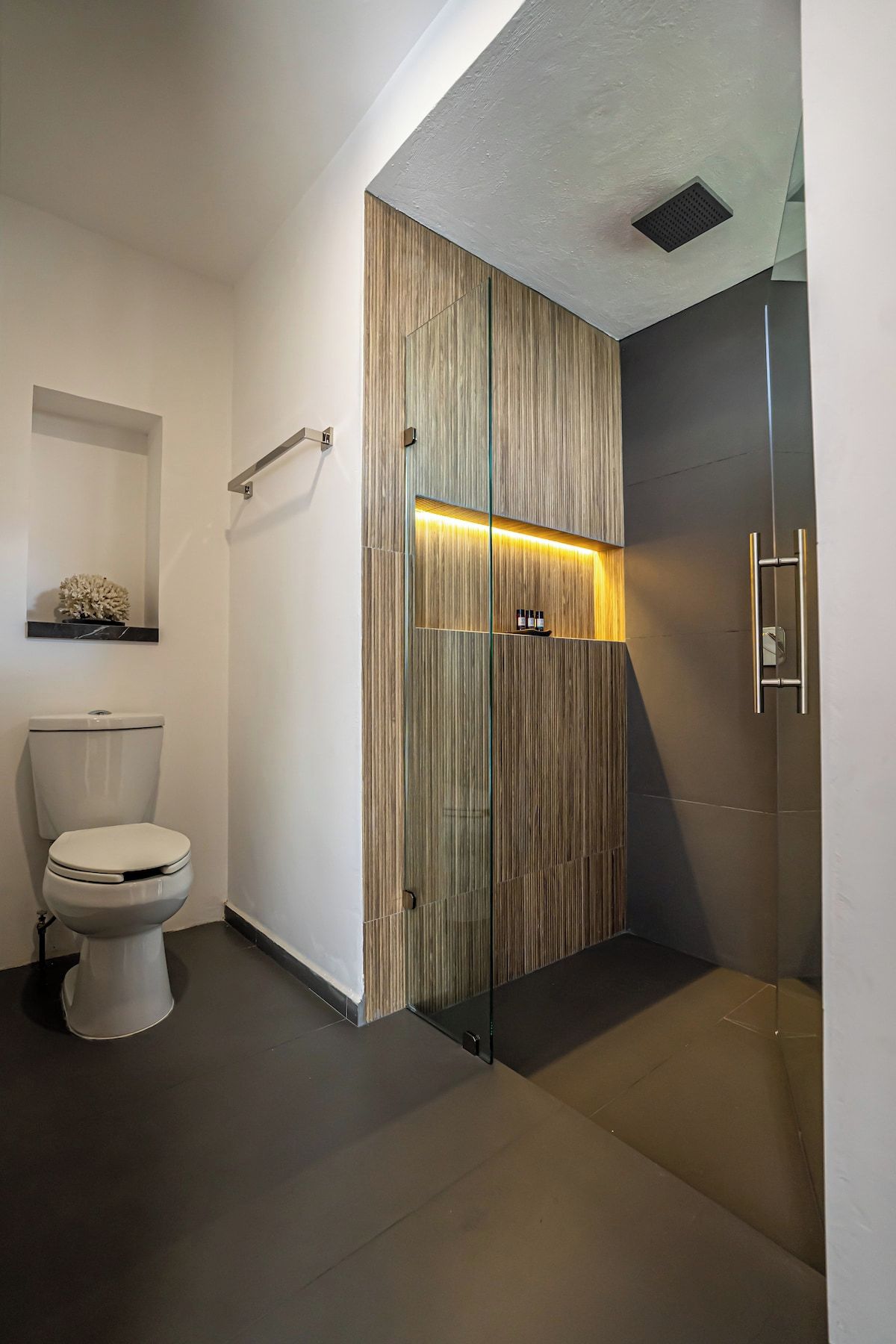 Un bagno moderno con il water, uno spazio doccia in vetro e un mobile lavabo in legno con luce integrata.