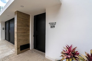 Ein moderner Gebäudeeingang mit einer Wand aus Holz, einer schwarzen Tür und einem Schild mit der Aufschrift 'PRIVADA DE LAURELES 109'.