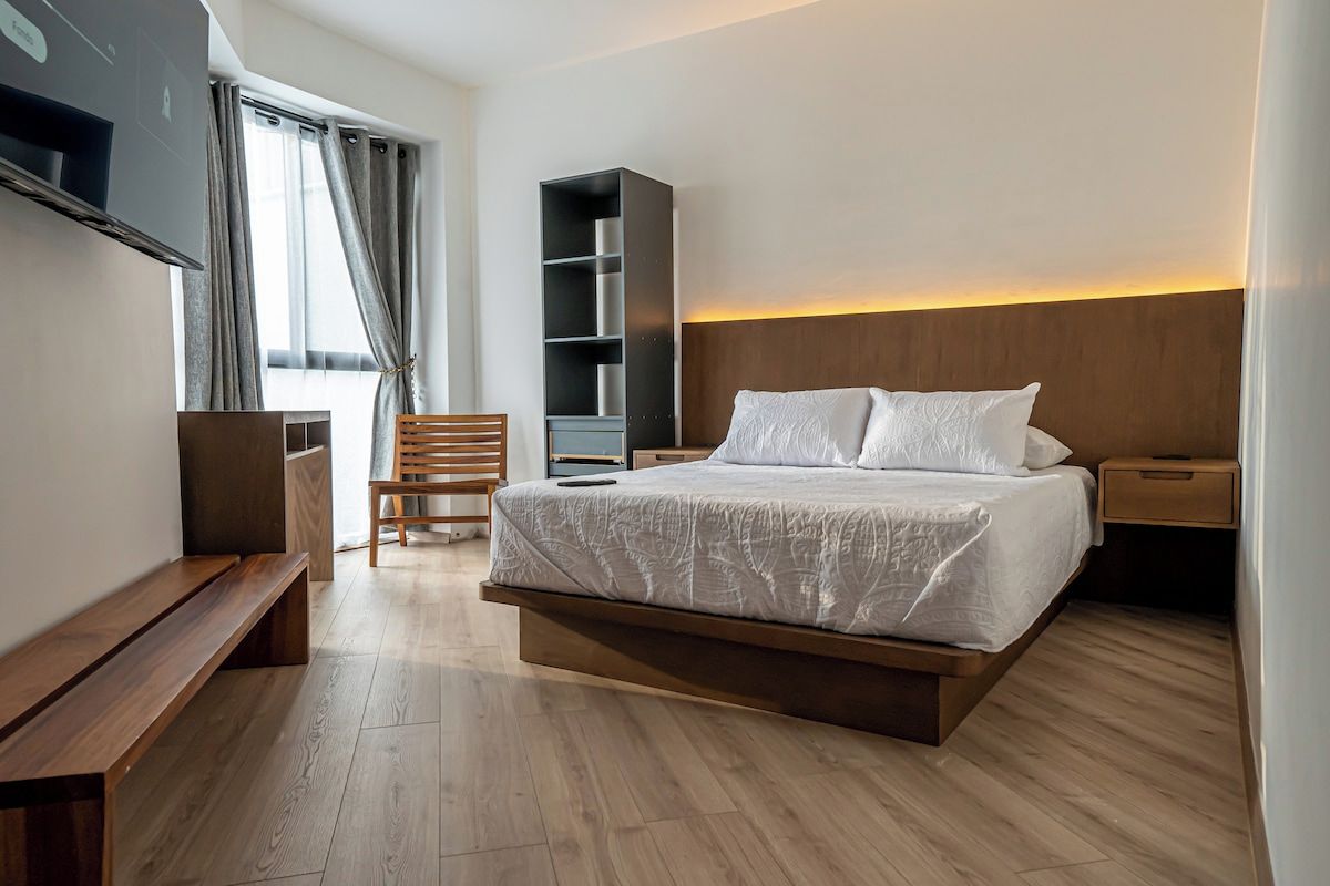 Moderni hotellihuone, jossa on suuri sänky, puinen penkki, televisio, kirjahylly ja työpöytä.