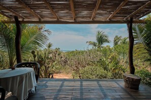 Eine Holzterrasse mit Tisch und Stühlen, die auf eine dichte tropische Landschaft mit Kakteen und Palmen blickt.